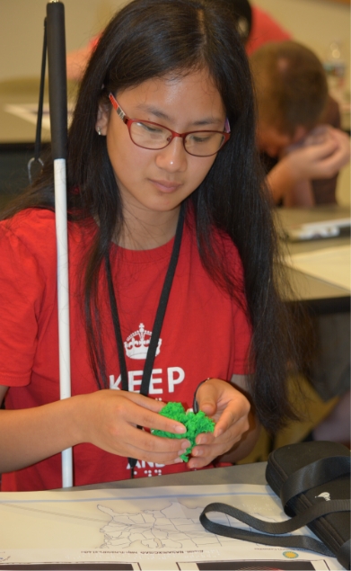 Photo of an Asian American female student who is low vision exploring 3D printed astronomy models with her hands.
