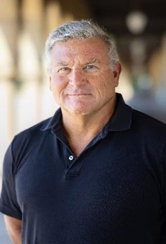 Portrait style photo of Roger Romani. The man has somewhat close-cropped grayish hair and he's wearing a navy blue polo shirt.
